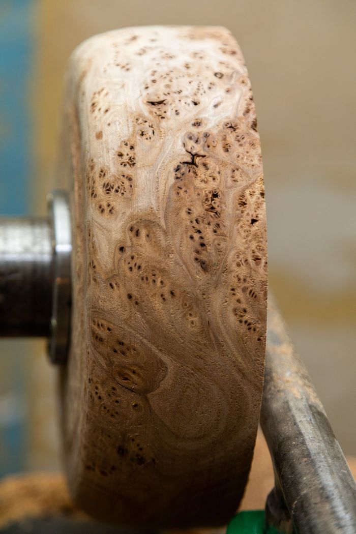 services-02 Detailed view of a wooden piece being crafted on a lathe, showcasing wood grain.