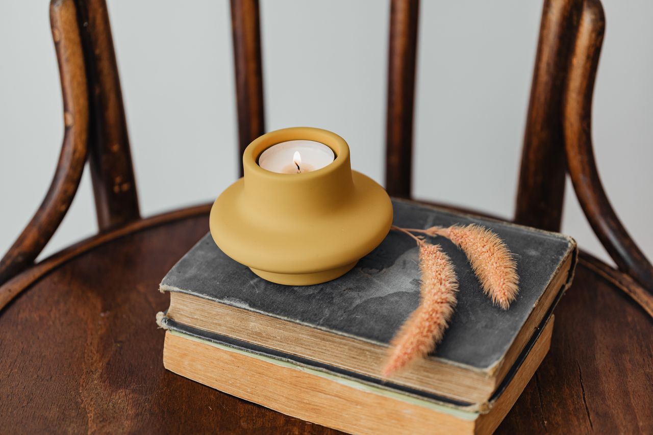 our-story Warm candle on vintage books and wooden chair, evoking a cozy atmosphere.