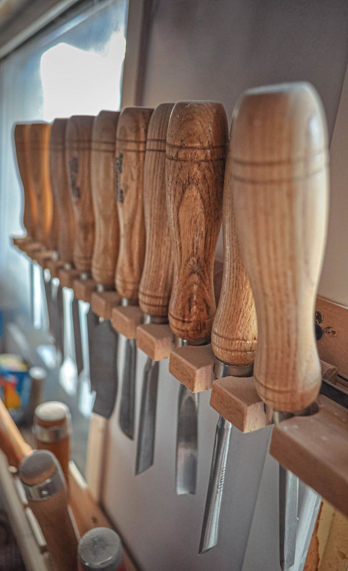 services-01 Close-up of wooden-handled chisels neatly arranged in a vertical storage rack in a workshop.